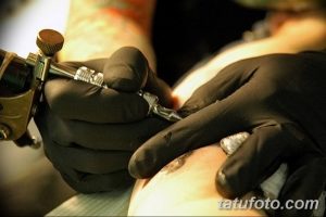 Фото тату: рука мастера в черных перчатках наносит татуировку. Крупный план процесса татуирования.